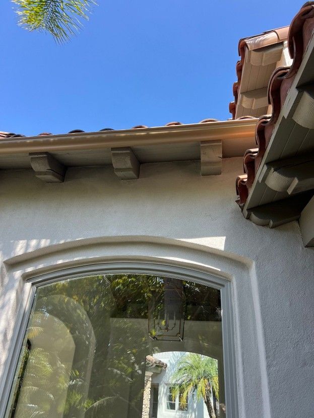 Stucco house exterior with arched window, terracotta roof tiles, and blue sky above