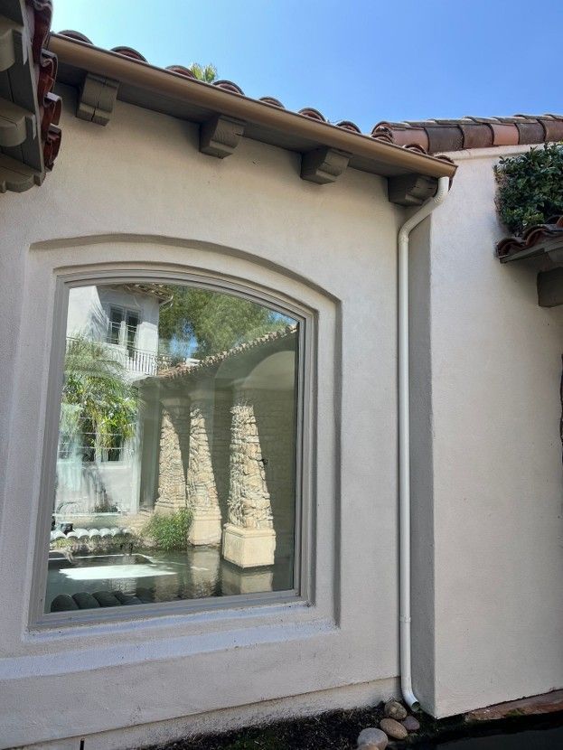 Stucco house exterior with arched window, tiled roof, and palm tree reflections