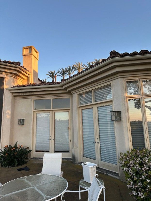 Patio with white metal table and chairs beside a beige stucco house with blue sky above