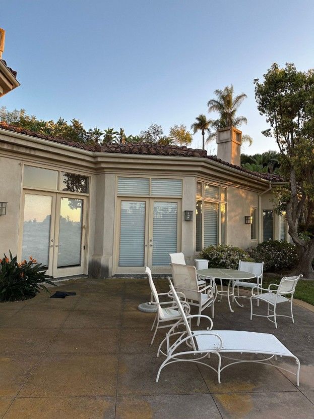 Patio with white lounge chairs and table outside a stucco house at sunset
