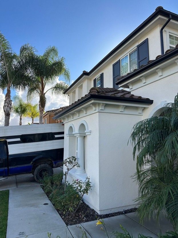 White stucco house exterior with arched trim, black SUV in driveway, and palm trees along the side.