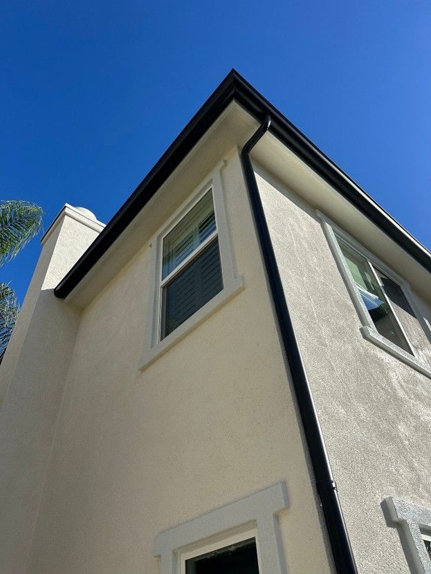 Corner of a cream house with black trim against a bright blue sky