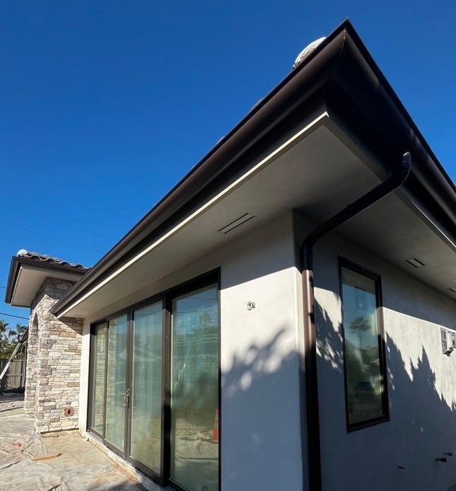Modern house exterior with large glass sliding doors and a dark roof under a blue sky