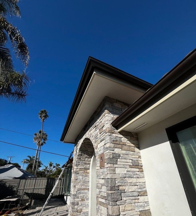 Modern house exterior with stone chimney, white siding, and a bright blue sky