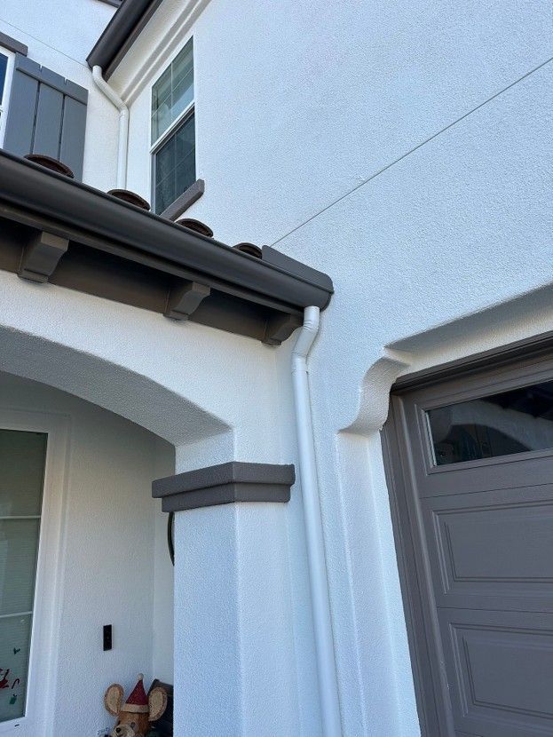 White stucco house exterior with arched entryway, gray roof trim, and windows in bright daylight