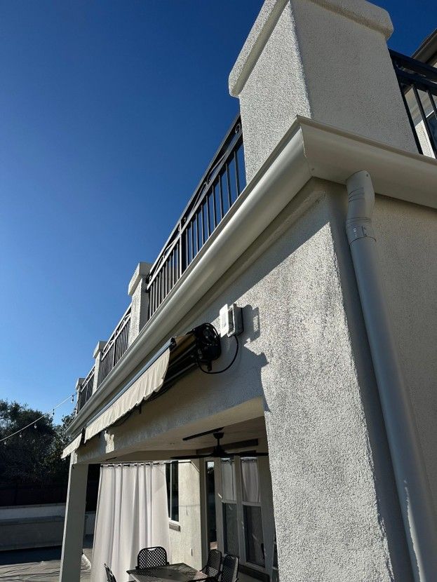 Exterior view of a house balcony with beige awning and white stucco walls under a blue sky