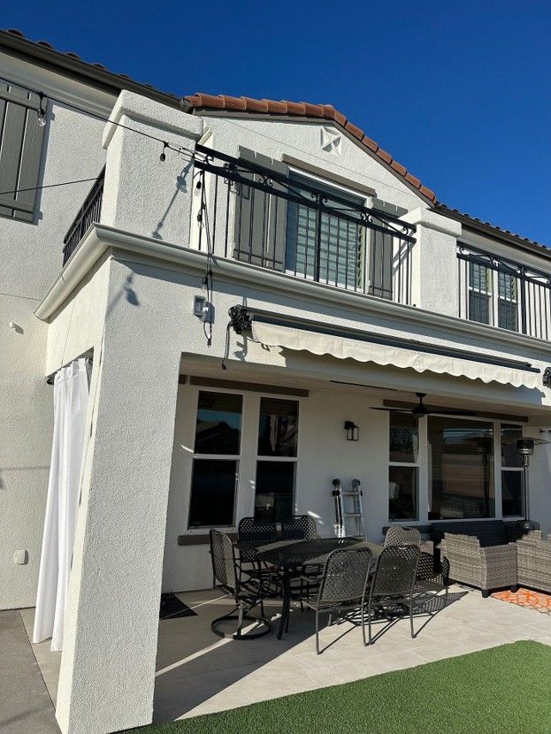 Two-story white house with a balcony, awning, and patio furniture under a clear blue sky