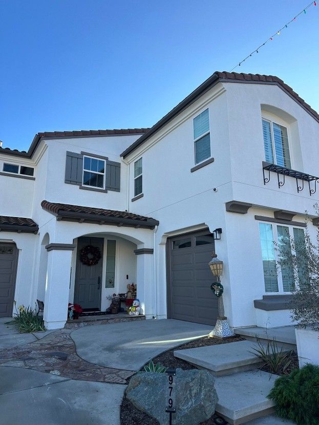 White two-story stucco house with a tiled roof, garage, and front steps under a clear blue sky