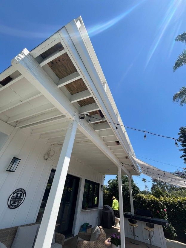 White porch roof and siding under a bright blue sky, with hanging string lights and a hillside view