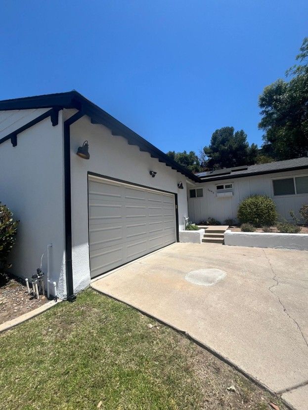 Driveway and attached garage with white siding, gray door, and concrete patio under a clear blue sky