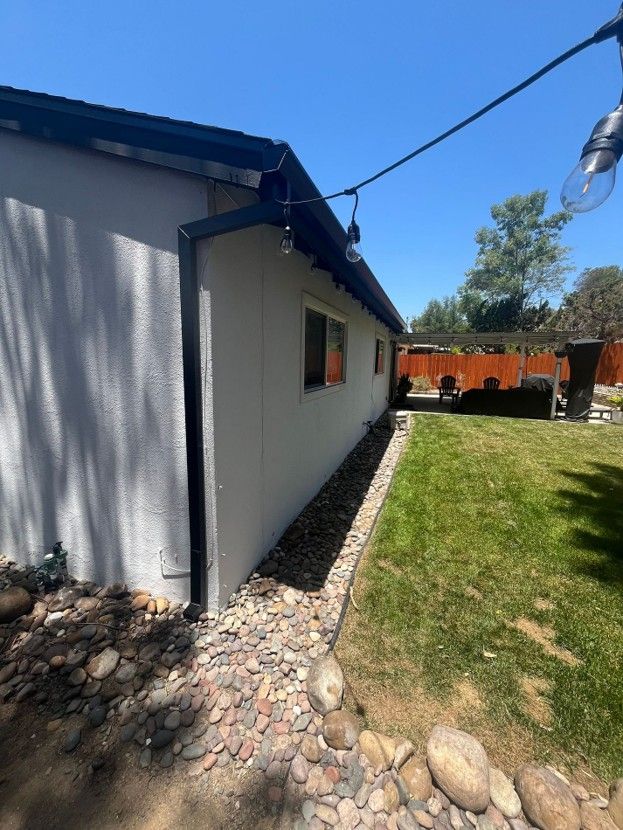 Side yard of a house with white siding, rock border, green lawn, and blue sky.