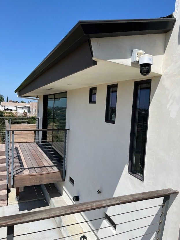 Modern house balcony with white walls, black trim, glass railings, and a security camera.