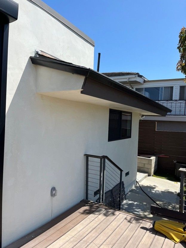 White stucco house exterior with a slanted roof, small stair railing, and a sunny backyard patio.
