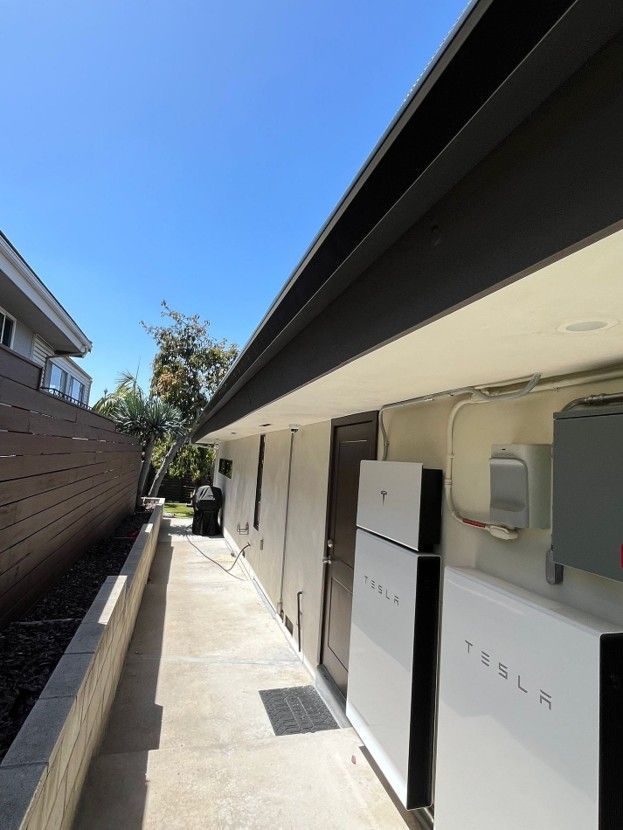 Outdoor utility corridor beside a building, with white electrical cabinets and a narrow walkway under blue sky