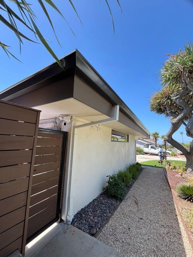 Side yard with white house wall, brown fence, gravel path, and blue sky
