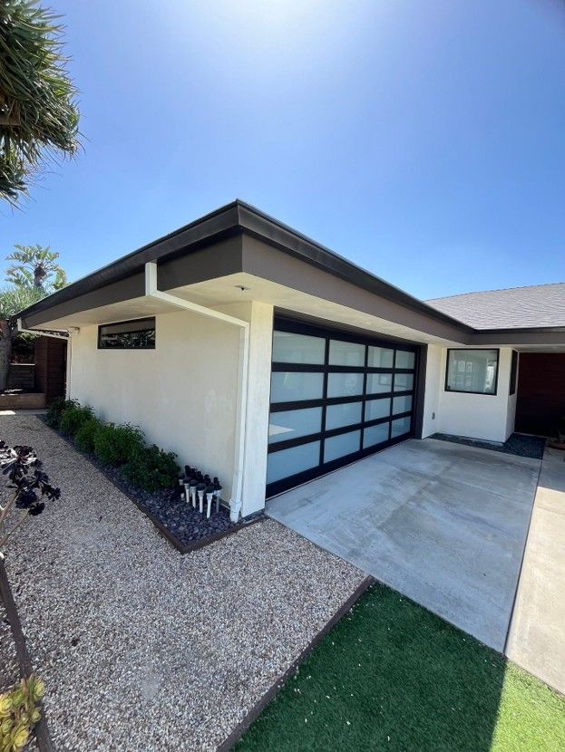 Modern white house exterior with black-framed garage door, concrete driveway, and gravel landscaping