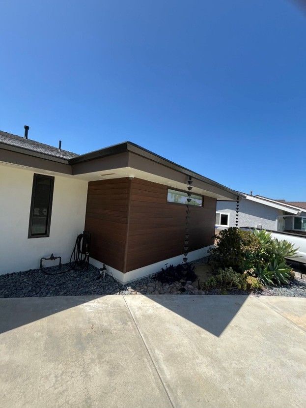 Single-story house exterior with wood siding, concrete driveway, and clear blue sky