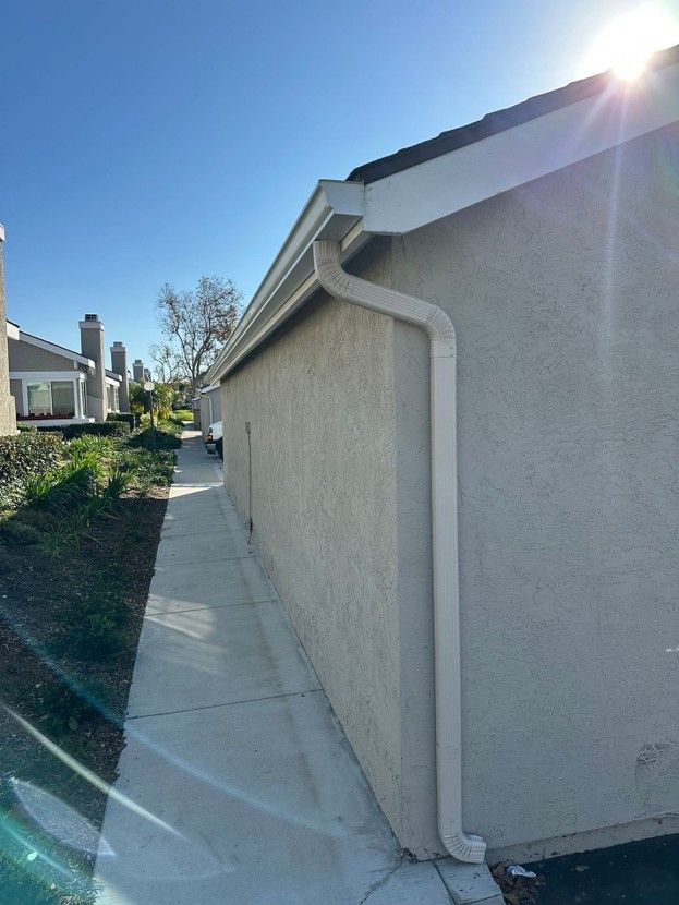 Narrow concrete side yard beside a beige house on a sunny day, with a sidewalk and blue sky.