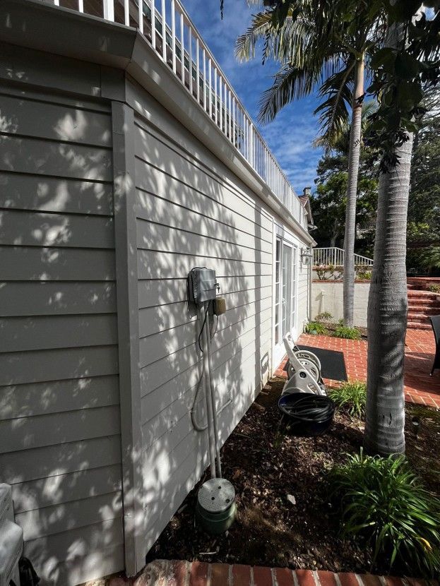 Side of a white house with palm trees, a garden bed, and a screened patio in the background.