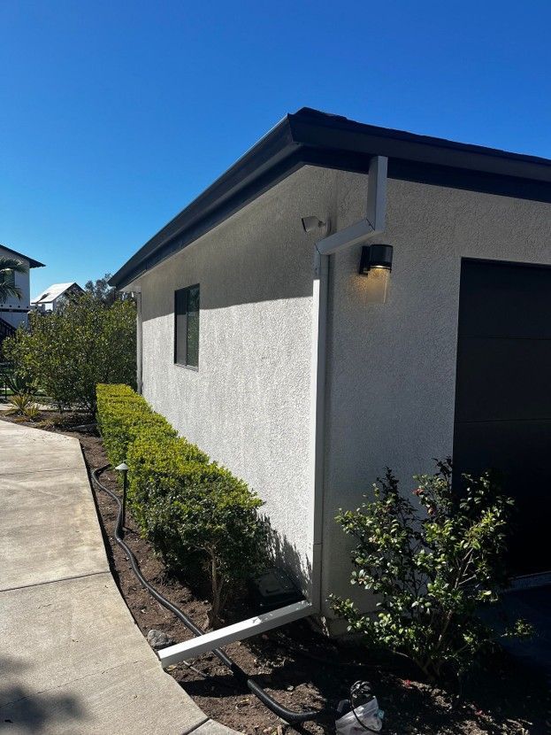 Side view of a stucco house with a walkway, trimmed shrubs, and a bright blue sky