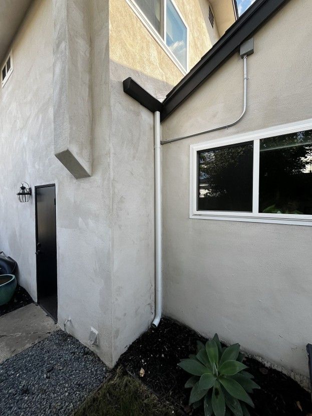 Exterior corner of a stucco house with a window, side door, gravel, and a small plant bed