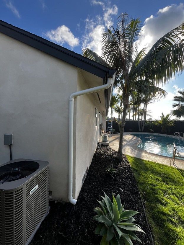 Backyard beside house with air conditioner, white downspout, palm trees, and swimming pool at sunset