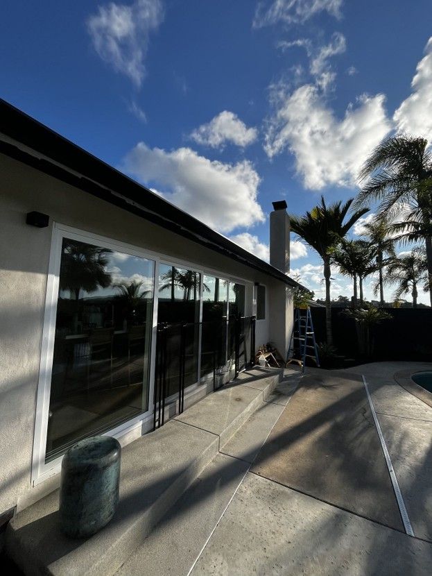 Modern house patio with glass doors, palm trees, blue sky, and a ladder by the chimney