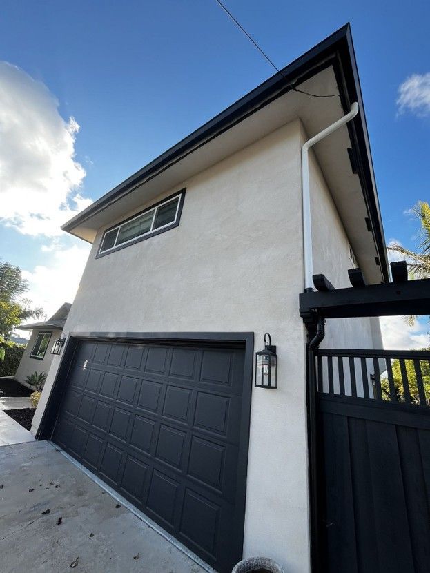 Modern white two-story house with black garage door and gate, viewed from a driveway