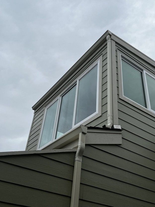Gray house corner with large windows and sloped roof against an overcast sky