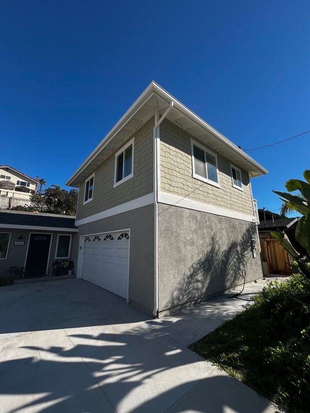 Two-story beige garage with white doors and driveway under a clear blue sky