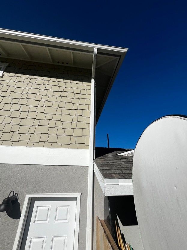 Exterior of a beige house with gray trim, white door, and bright blue sky, beside a large white curved structure
