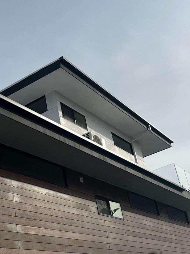Modern house exterior with dark wood siding and white upper walls, viewed from below under a cloudy sky