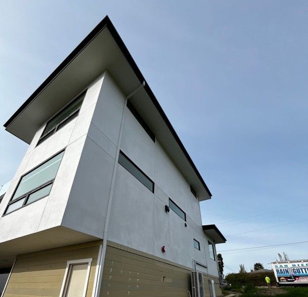 Modern white house with a steep dark roof viewed from below under a blue sky