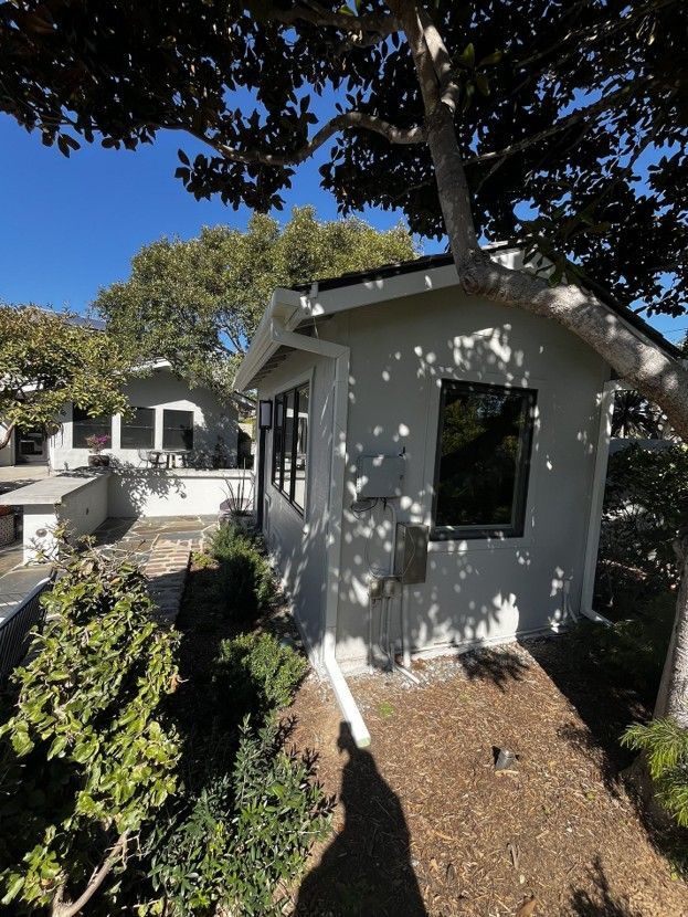 White house exterior with black-trimmed windows and trees casting shadows in a sunny yard