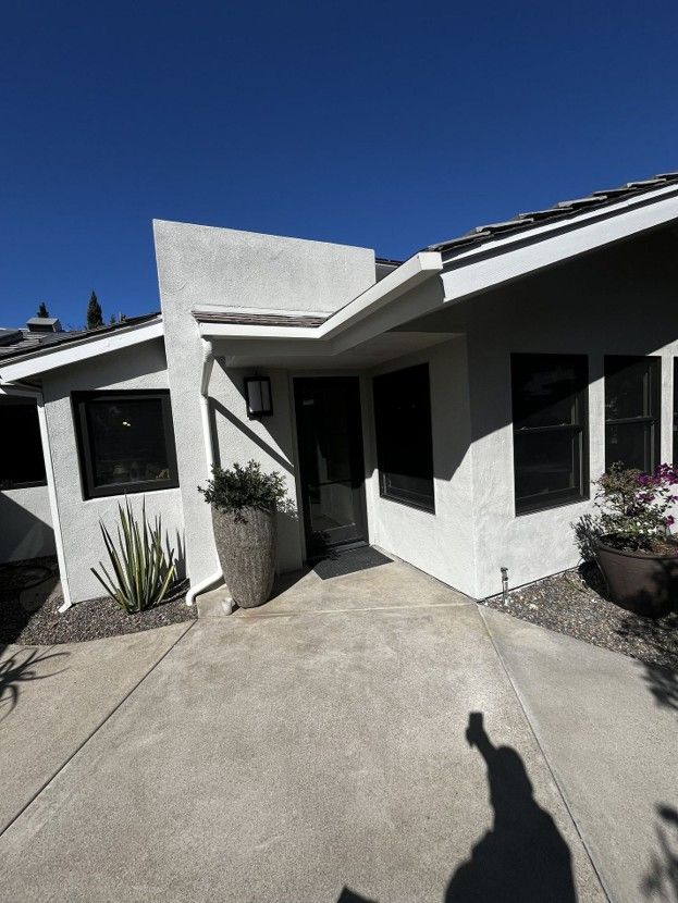White stucco house entrance with a concrete walkway, black-framed windows, and blue sky overhead