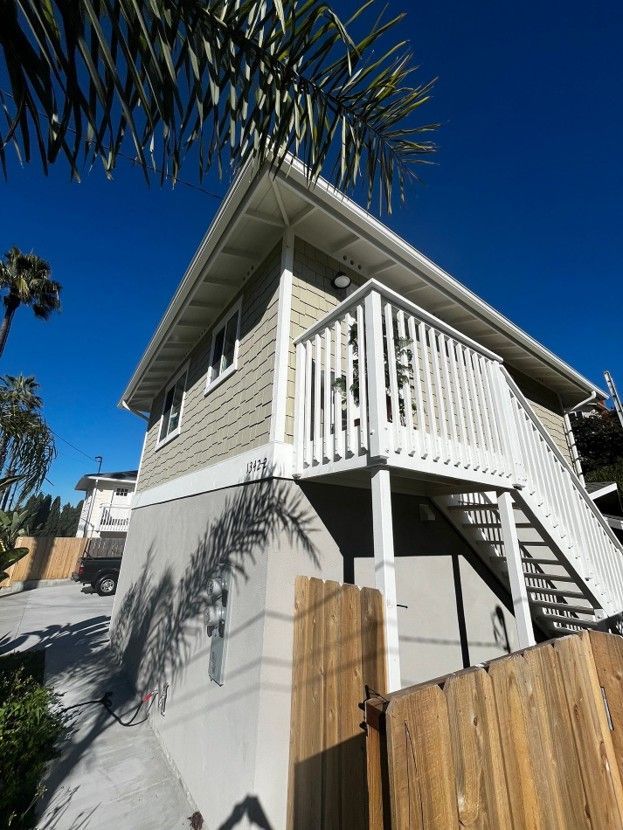 Two-story house with white balcony and stairs, viewed from below against a blue sky