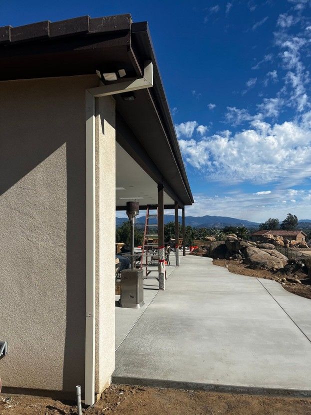 Side of a house with a concrete patio, desert landscaping, and mountains under a blue sky.