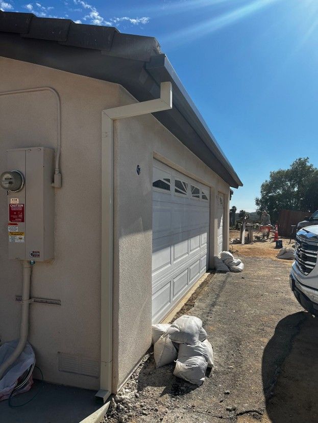 Side view of a stucco house with a white garage door, gravel driveway, and parked truck under a bright blue sky