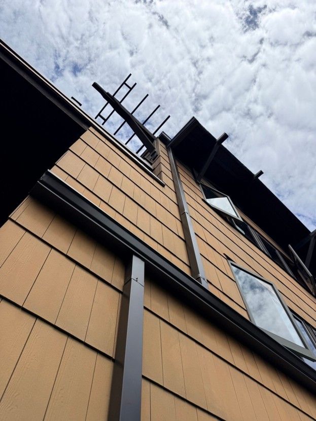 Low-angle view of a tan building with a ladder against it under a cloudy sky