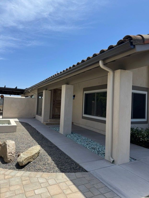 Modern single-story house patio with beige columns, tiled roof, and a gravel courtyard under a blue sky
