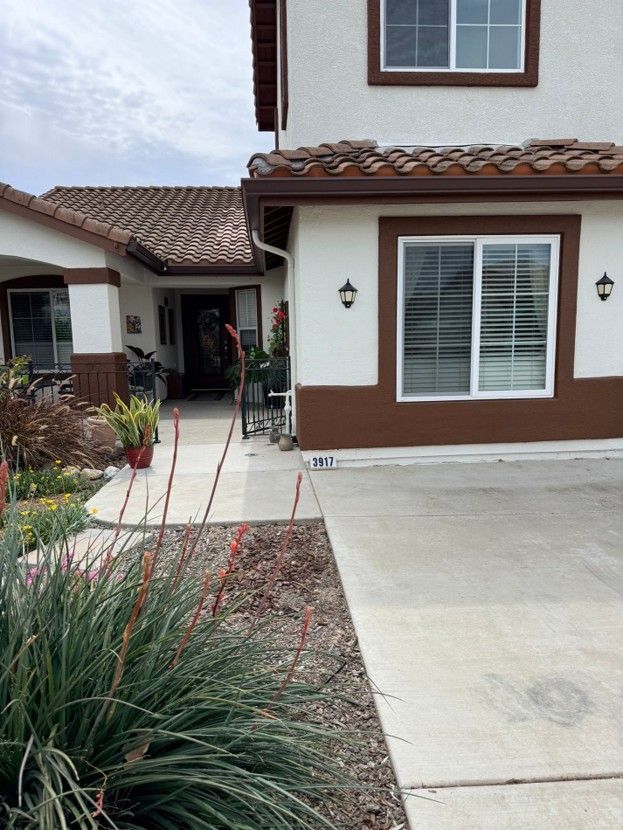 Suburban house exterior with a white and brown facade, driveway, walkway, and desert landscaping
