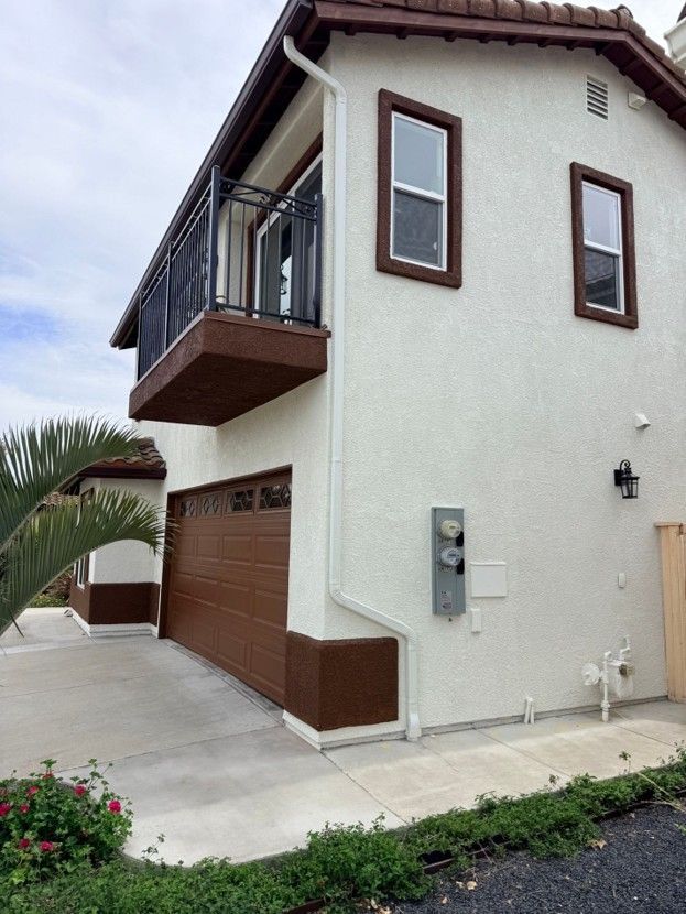 Two-story beige house with brown trim, balcony, garage, and driveway