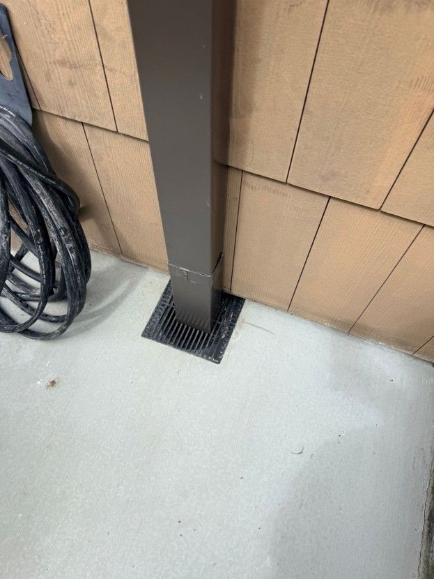 Coiled black cable beside a dark post anchored to tan siding on a light concrete floor.