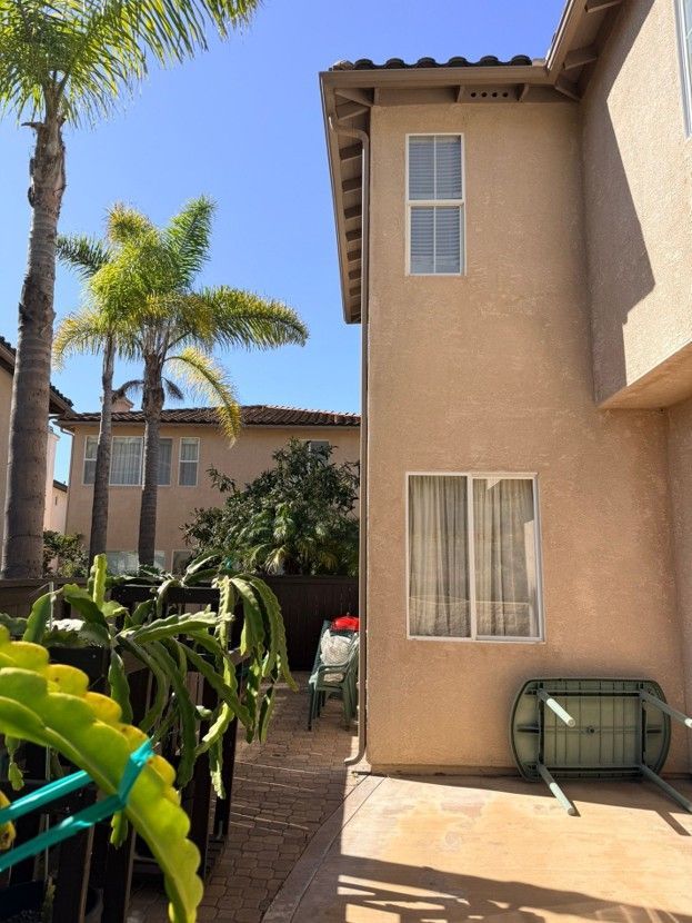 Backyard patio beside beige stucco house with palm trees and outdoor storage bench