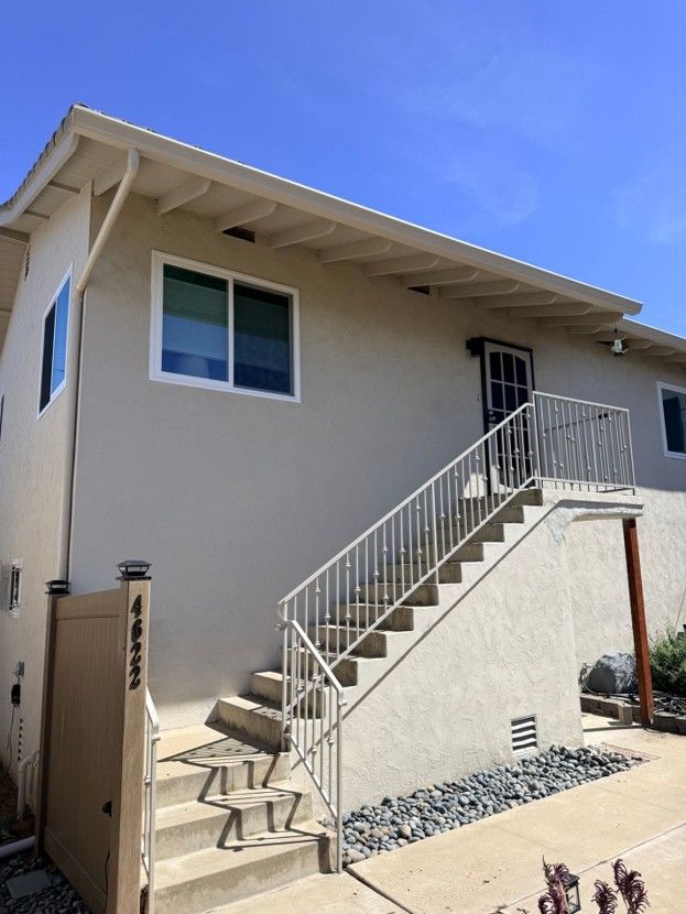 Exterior of a beige house with white stairs and railing under a blue sky