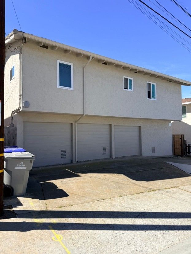 Two-story beige townhouse with three garage doors, windows, and a sloped driveway under clear blue sky