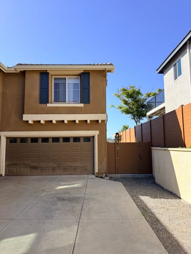 Two-story tan house with brown garage door and driveway under a clear blue sky