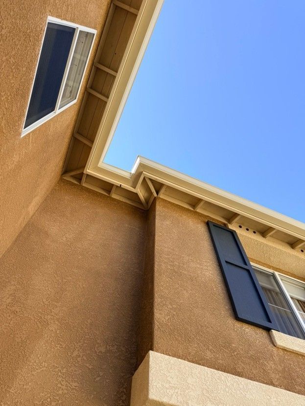 Upward view of tan stucco apartment building with dark shutters against a blue sky