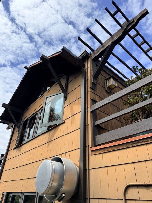 Tan house exterior with window, metal fence, and roof beams against a blue sky