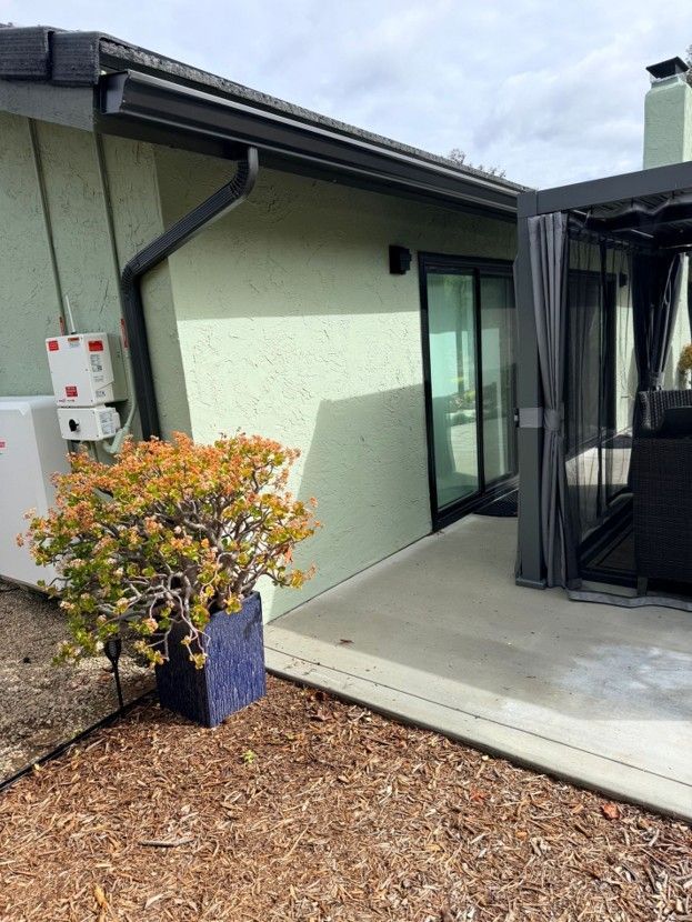 Patio beside a house with a potted shrub, sliding glass door, and black screened enclosure.